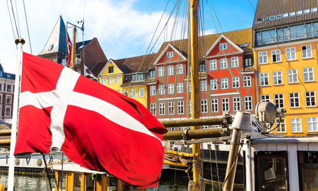 Denmark's national flag flying in the foreground of Copenhagen's famous old Nyhavn port.