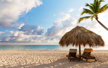 Beach chairs with umbrella and beautiful sand beach in Punta Cana, Dominican Republic (Photo via Preto_perola / iStock / Getty Images Plus)