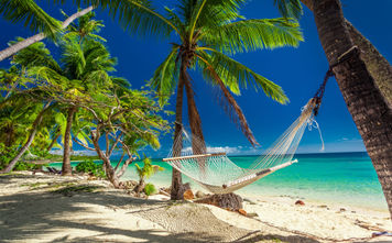 Empty hammock in the shade of palm trees on tropical Fiji Islands (photo via mvaligursky / iStock / Getty Images Plus)