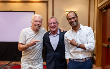 John Lovell (center) poses with Virgin Voyages founder Richard Branson (left) and CEO Nirmal Saverimuttu (right)