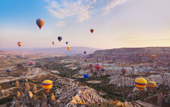 Hot air balloon flying over rock landscape at Cappadocia Turkey (photo via TPopova / iStock / Getty Images Plus)